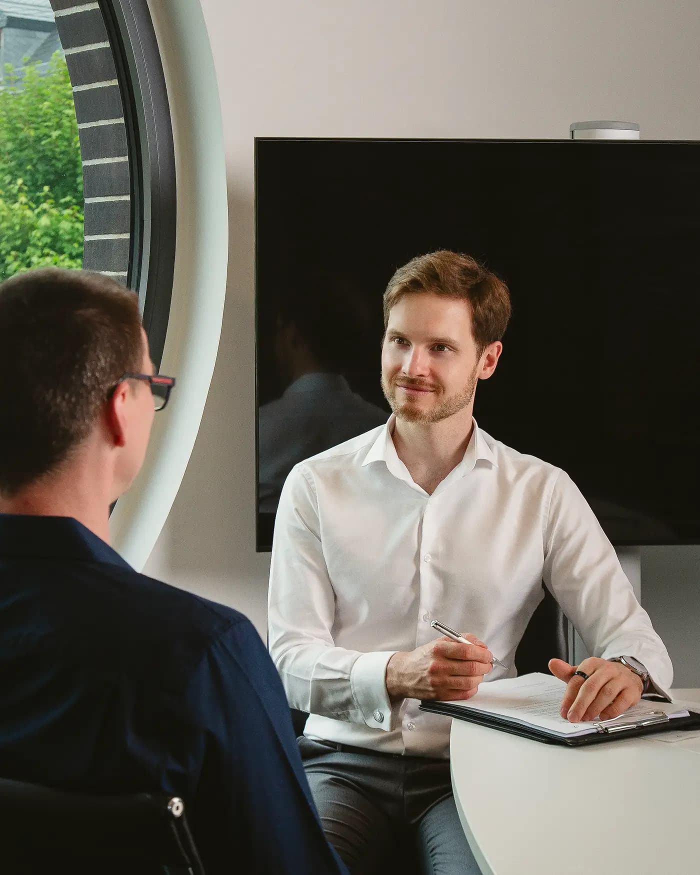 Dieselbe Szene am runden Tisch im Licht des Rundfensters; der Seminarleiter macht sich Notizen.